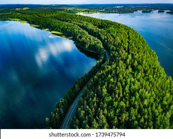 Vista aérea de la carretera con coches entre bosque verde y agua del lago azul en verano Finlandia