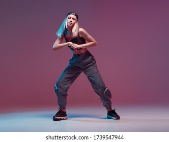Una linda adolescente bailando hip-hop con ropa elegante, una gorra de béisbol, en un estudio con luces de neón. Afiche de color de baile.