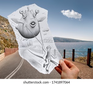 Lustige Fantasy-Kreatur, die mit einem Seil gehalten wird, von einem laufenden Jungen, der auf einem handgehaltenen Blatt Papier mit Meereslandschaft in Santorini im Fotohintergrund gezeichnet ist. Mixed-Media-Bild.