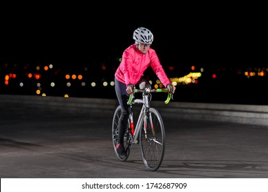 Young Woman Cyclist Riding Road Bike. Night City Lights at the Background. Healthy Lifestyle and Urban Sport Concept.