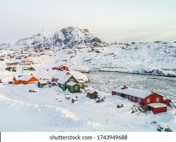 Coloridas casas inuit en la ciudad ártica de Groenlandia Sisimiut enterradas en la nieve durante el frío y helado invierno con bajo brillo solar y colinas rocosas con montañas empinadas y altas en el fondo y bahía congelada