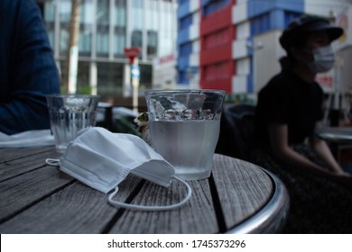 A protective mask lies on a table in a cafe and next to it is a glass of water. Masks can cause dehydration and difficulty breathing in hot weather. When you wear a mask in the summer you need water.