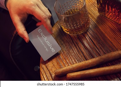 La mano del hombre pone la tarjeta de membresía exclusiva sobre la mesa. La mano de un caballero pone una tarjeta de membresía exclusiva en la mesa de madera con whisky en una jarra y un vaso con puros.