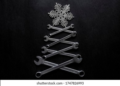 抽象的なクリスマス ツリーは、黒い背景の上に雪だるまとレンチで作られました。工業用のクリスマス、冬、新年のコンセプト。家の装飾。メカニック、便利屋のグリーティング カードのコンセプトです。
