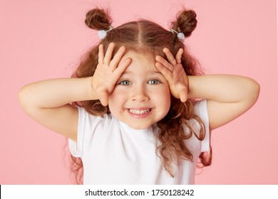 Retrato de niño pequeño lindo sorprendido niña sobre fondo rosa. Mirando a la cámara. Señala con las manos hacia el lado izquierdo. Publicidad de productos para niños