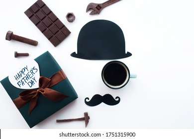 Father's Day Holiday Concept. Flatlay. Hat, coffee mug, gift, chocolates in the form of old tools and a funny black mustache on an isolated white background. Copy space for inscriptions.