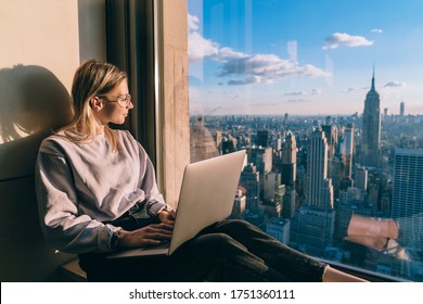 Blanke vrouw in trendy kleding die in het raam kijkt op het grootstedelijke centrum bewondert de schoonheid van boven New York, duizendjarige vrouwelijke blogger met laptopcomputer die denkt aan een inhoudsidee voor het delen van internet