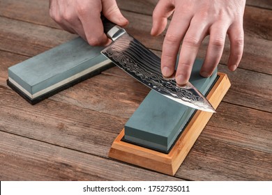 Homem afiando uma faca de chef japonesa com uma pedra de amolar molhada sobre uma mesa de madeira rústica.