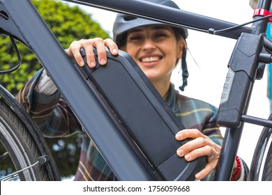 jonge vrouw die een elektrische fietsbatterij vasthoudt die op het frame is gemonteerd