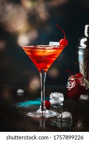 Manhattan alcoholic cocktail with bourbon, red vemuth, bitter, ice and cocktail cherry in glass, night mood image, copy space
