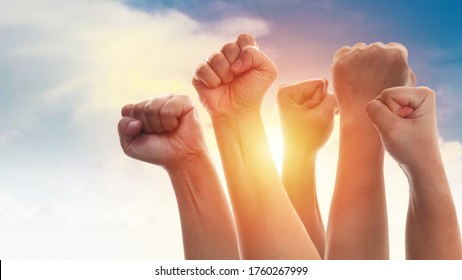 劇的な青空に太陽の光、怒り、抗議、革命、インスピレーション、モチベーション、チームワークのコンセプトを背景に、男性と女性の大人の拳が立ち上がる
