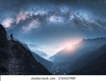 Voie lactée arquée, femme et montagnes la nuit. Silhouette d'une fille debout sur le sommet de la montagne, montagnes dans des nuages ​​bas et ciel étoilé au Népal. Paysage spatial avec une arche lumineuse de la Voie lactée. Voyage