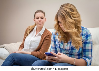 スマートフォンでメッセージを見ながら、10 代の娘をスパイしている不審な母親。新技術による悪い家族コミュニケーションの概念