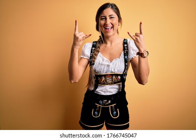 Jonge mooie brunette duitse vrouw die Oktoberfest viert in traditionele kleding die schreeuwt met een gekke uitdrukking die rocksymbool doet met de handen omhoog. Muziek ster. Zwaar muziekconcept.