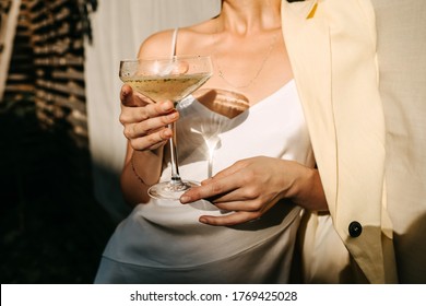 Luxe vrouw, gekleed in een witte jurk, met een coupe met champagne in zonlicht. Concept van een openluchtfeest.