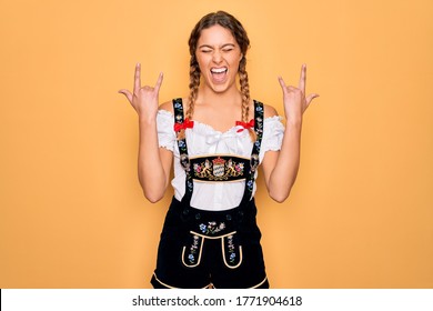 Young beautiful blonde german woman with blue eyes wearing traditional octoberfest dress shouting with crazy expression doing rock symbol with hands up. Music star. Heavy music concept.