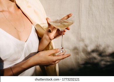 Mujer joven con un vestido blanco, sosteniendo una copa de champán a la luz del sol. Concepto de fiesta al aire libre.