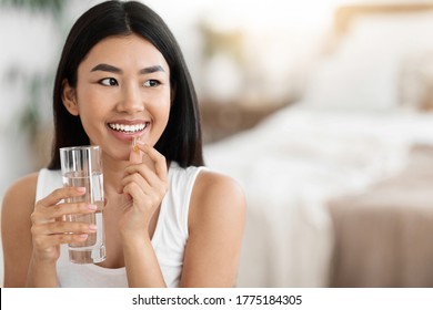 Diet, nutrition, healthy eating concept. Close Up Of Happy Smiling Asian Woman Taking Supplement Pill And Holding Glass Of Fresh Water In Morning, copy space