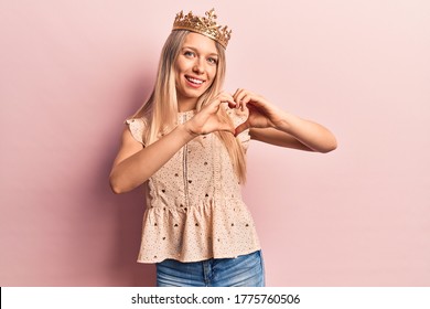 年轻的金发女郎戴着公主皇冠，满脸爱意地微笑着，用双手展示着心形的符号和形状。浪漫的概念。