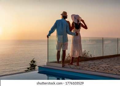 A romantic couple with hats on vacation time enjoys the summer sunset by the pool