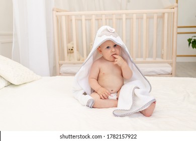 baby boy 8 months old sitting on a white bed in a white towel after bathing in the bathroom at home, place for text
