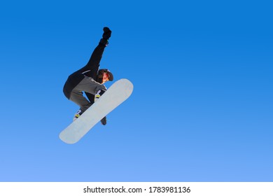 Gadis snowboarder melakukan trik melompat dengan pegangan di langit biru. Latar belakang gradien biru mengisolasi atlet dalam penerbangan