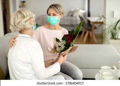 Adult daughter bringing bouquet of flowers to her mother while vising her during coronavirus epidemic. 