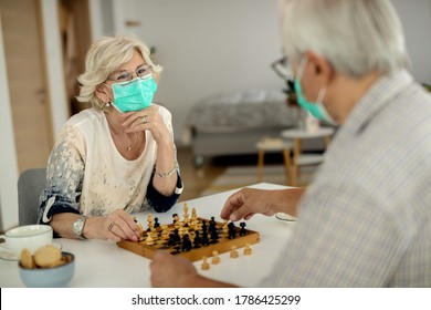 家でチェスをしている間、年配の女性と彼女の夫は防護マスクを着用しています。