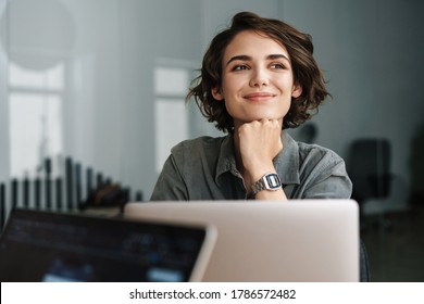 Imagen de una joven hermosa y alegre mujer sonriendo mientras trabaja con una laptop en la oficina