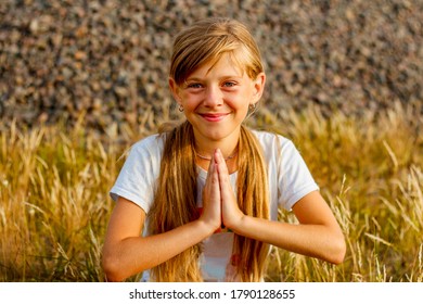 Happy little girl folded her hands in palm hand in front of chest, sincerely believes fulfillment to dreams, makes wish. prayer concept for faith, spirituality and religion. Practicing meditate yoga