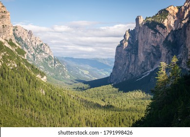Valle montañoso posglacial en forma de U en las Dolomitas italianas. En el fondo, entre paredes rocosas y escarpadas, crecen bosques verdes. La foto fue tomada en un día soleado de verano durante la caminata por la Alta Vía.