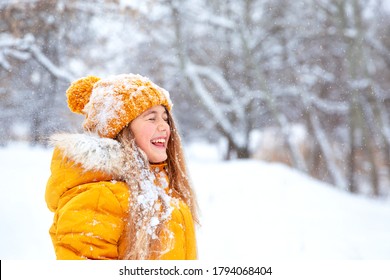 Buitenportret van een close-up van een jong, mooi, vrolijk lachend meisje, gekleed in een geel jasje en een gebreide muts, wandelend in een winterpark