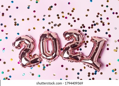 Gold pink balloons in form of numbers 2021 with colorful shiny confetti on pink background. Happy New Year celebration. Flat lay, top view