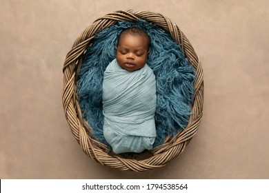Schläfrig gewickelter afroamerikanischer Neugeborener, der auf einem blauen Teppich in einem Korb mit Kopierraum liegt
