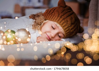 Mädchen in Strickmütze in der Nähe von Weihnachtsbaum macht einen Wunsch für neues Jahr. Glückliches kleines Mädchen aufgeregt an Heiligabend. Hoffnungskonzept Warten auf Weihnachtsmann. Hoffnungsvolles Kind. Silvester. Träume werden wahr.