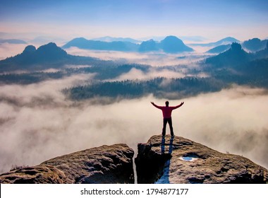 Pequeña silueta de excursionista disfrutando del hermoso amanecer en las montañas de la mañana. Viajero con las manos levantadas de pie en la montaña con niebla blanca debajo.
