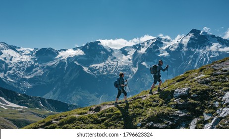 Dos jóvenes excursionistas (una pareja) caminando por una montaña en Austria en verano, con pintorescas montañas cubiertas de nieve en el fondo
