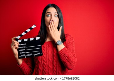 Sutradara muda wanita dengan mata biru membuat film sambil memegang papan berdinding merah menutupi mulutnya dengan tangan, terkejut karena malu karena kesalahannya, ekspresi ketakutan, takut dalam diam, konsep rahasia