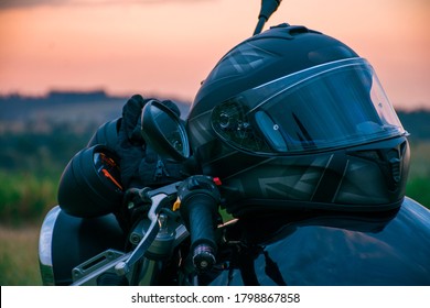 A black motorcycle helmet placed on the seat of a black motorcycle parked on the street with a natural landscape.