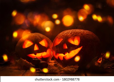 Halloween pumpkin head jack o lantern with burning fire background, wooden table  with light bokeh garland. Beautiful Holiday Autumn Composition