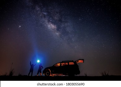 Manntourist mit Taschenlampe nachts nahe seinem Lagerauto. Raumhintergrund mit Rauschen und Körnung. Nachtlandschaft mit Auto und bunter, heller Milchstraße. Schöne Szene mit Universum.