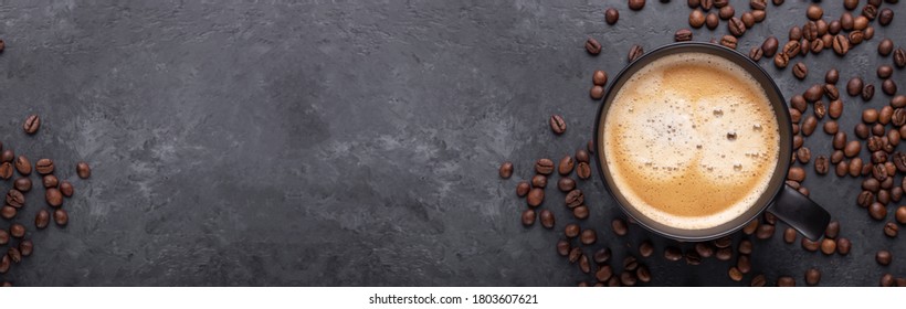 Spanduk horizontal dengan secangkir kopi dan biji kopi di latar belakang batu gelap. Pandangan atas. Salin ruang - Gambar
