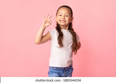 Estoy bien. Adorable niña asiática que muestra un gesto de aprobación aceptable en la pared del estudio rosa pastel, espacio de copia