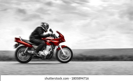 Seorang pengendara sepeda motor mengendarai sepeda motor berwarna merah dengan kecepatan tinggi. Hitam dan putih. Efek warna selektif