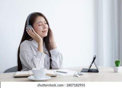 Young Asian woman happily listening to music in her private office, Relaxation by listening to music, Feel good concept.