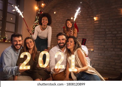 新年のパーティーで楽しんでいる若い友人のグループは、次の新年を表す照明番号2021を保持し、真夜中のカウントダウンで線香花火で手を振っています