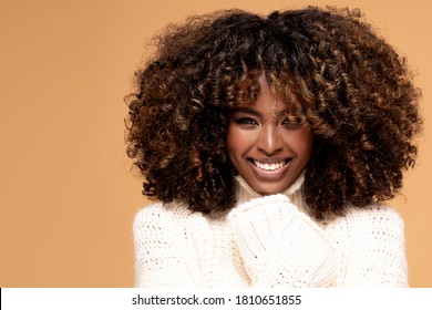 Feliz hermosa chica africana con peinado afro posando en un suéter acogedor sobre fondo de estudio beige.