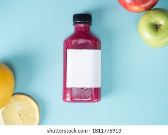 空のロゴラベルが付いたペットボトル容器に紫色のパステルカラーの飲み物。スタジオの背景に多くの野菜や果物のスムージー ジュースを混ぜた。ライム、青リンゴ、赤リンゴが飾られています。