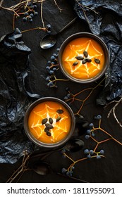Halloween pumpkin cream soup with creamy spider web sprinkled with pumpkin seeds in black bowls on a dark background top view