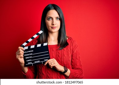 Sutradara muda wanita dengan mata biru membuat film sambil memegang papan berdinding merah dengan ekspresi percaya diri di wajah cerdas sambil berpikir serius